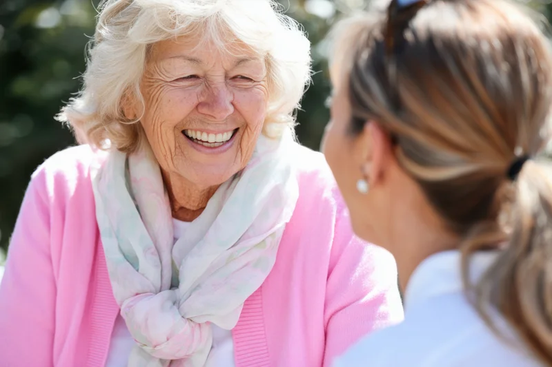 Elderly woman smiling warmly while chatting with another woman outdoors