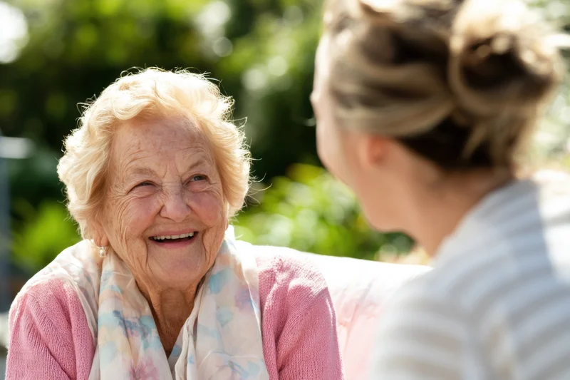 Elderly woman smiling while chatting with another woman in a garden