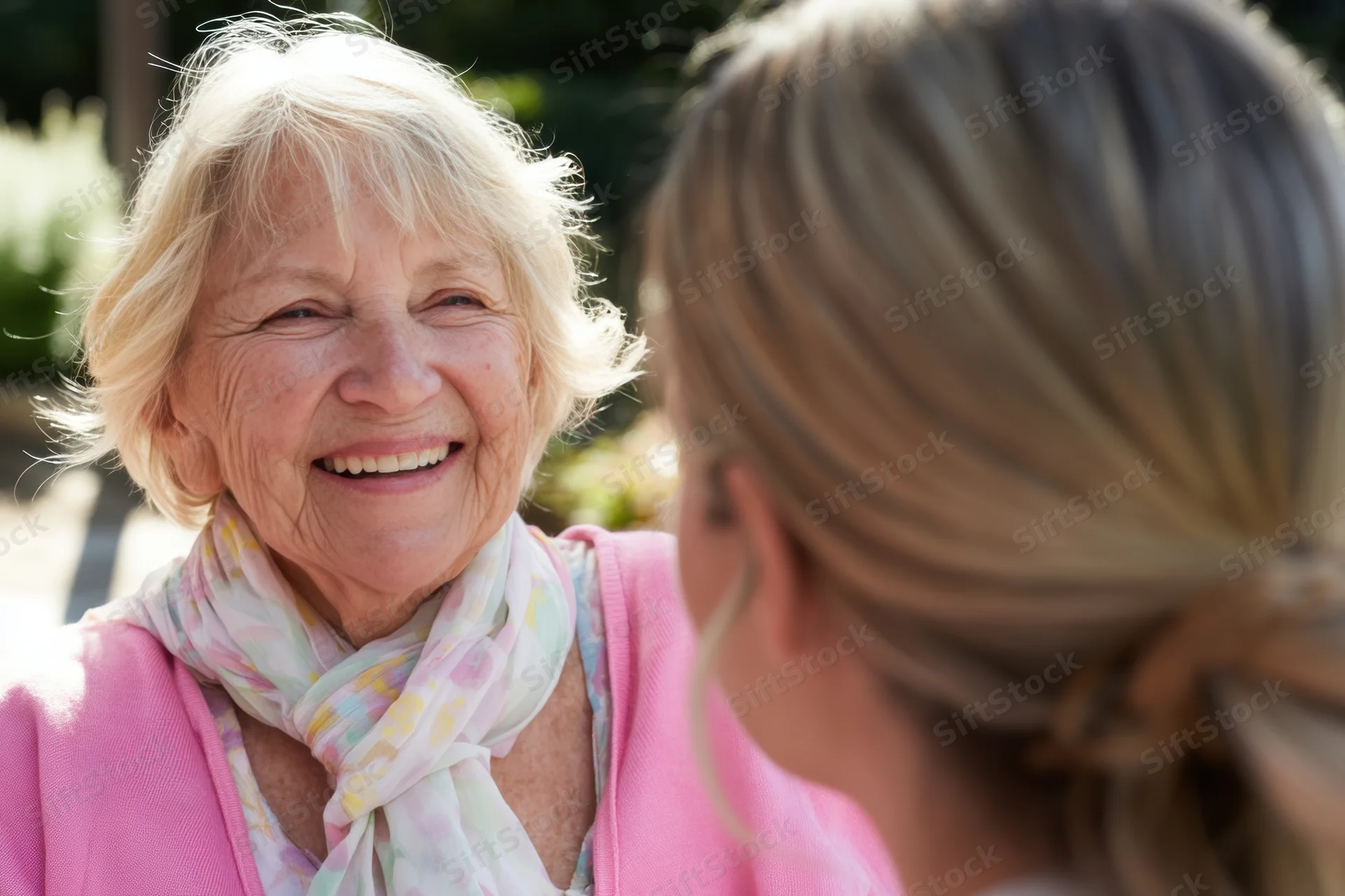 Elderly woman smiling warmly while chatting with a younger woman in a sunlit garden