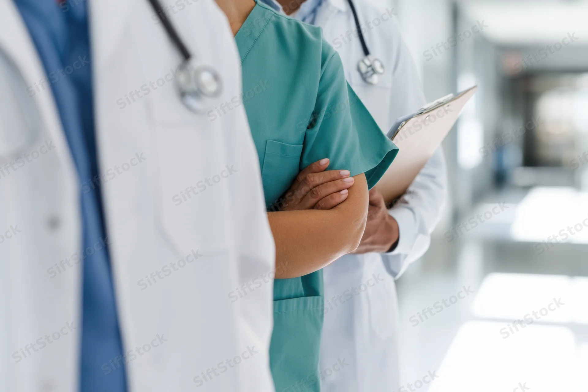 Doctors and a nurse standing in a hospital corridor with stethoscopes and a clipboard