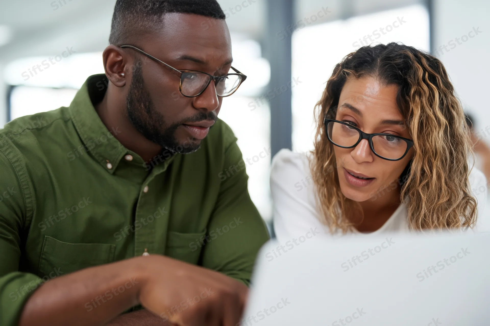 Two coworkers collaborating over a laptop in a bright modern office