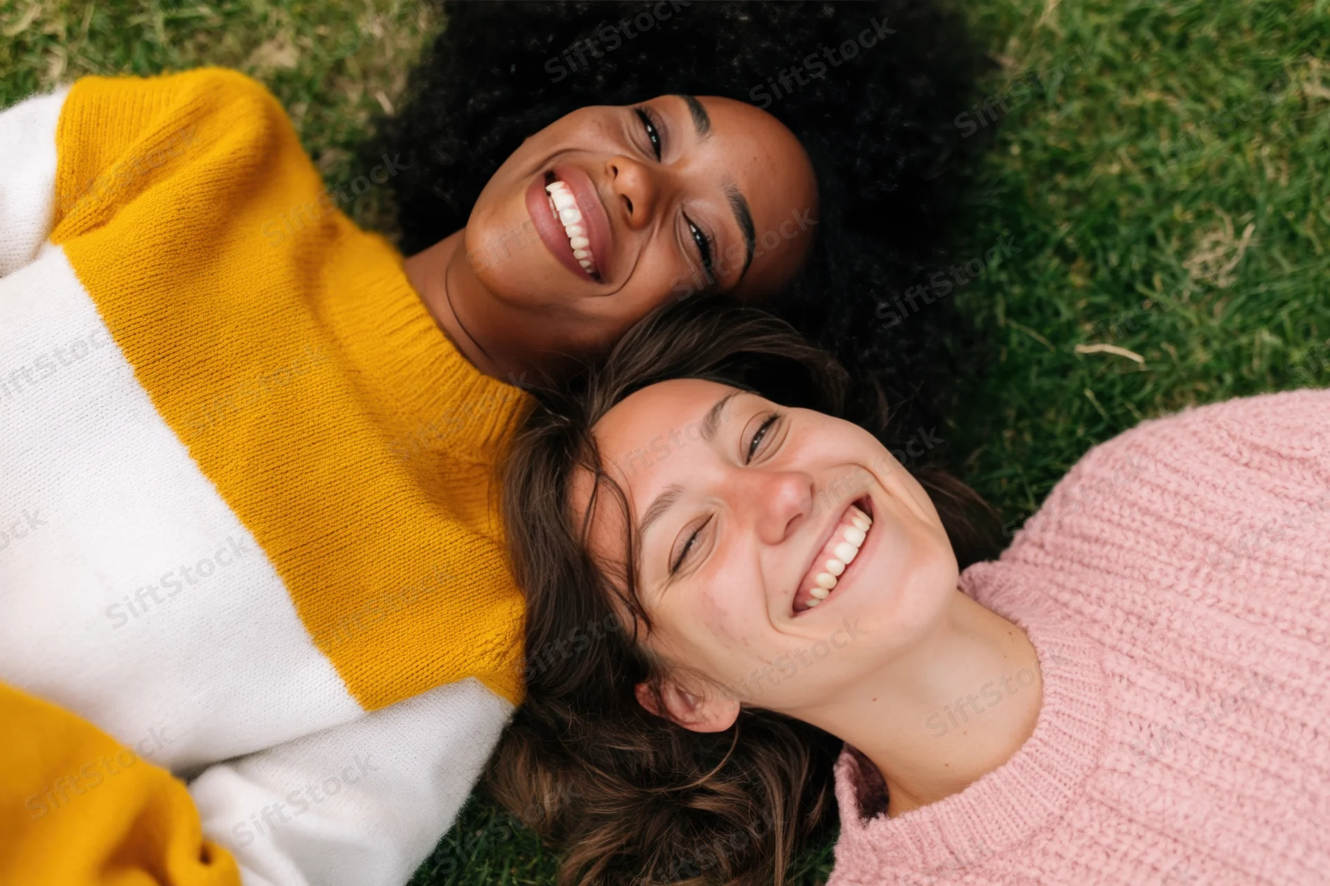 Two women lying on grass smiling up at the camera