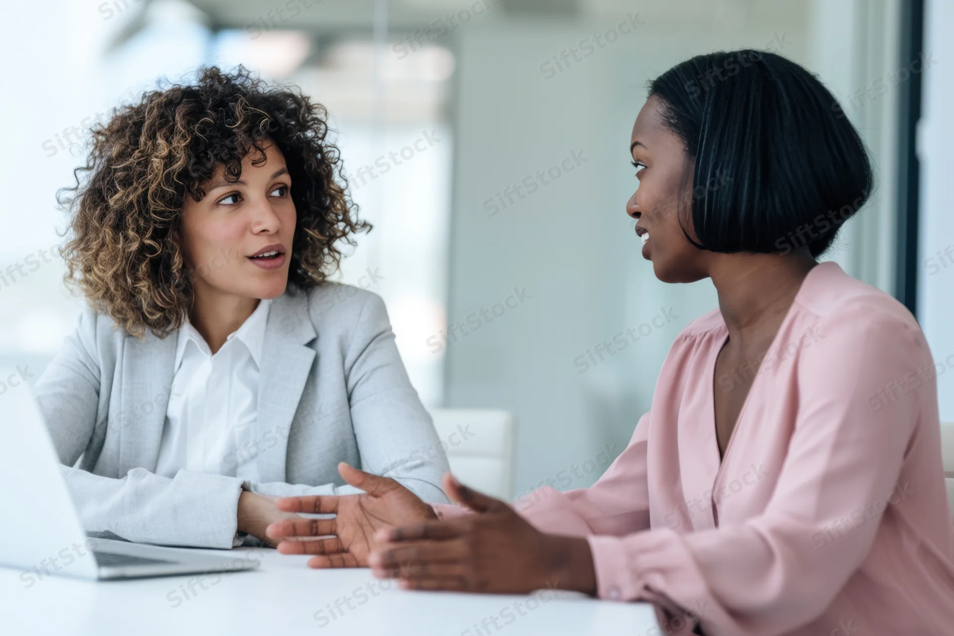 Two professional women conversing at a desk in a modern office