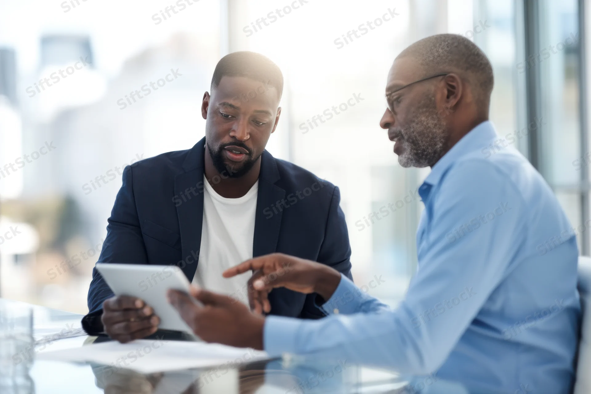Two men discussing a tablet during a meeting in a modern office