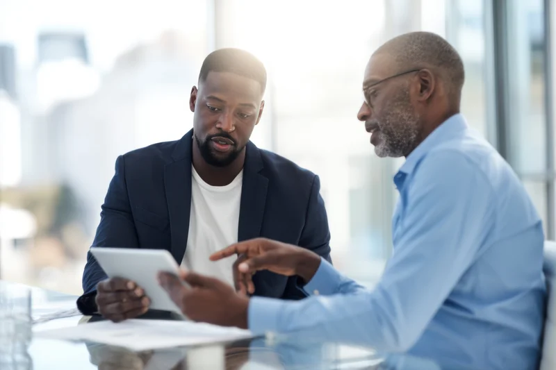 Two men discussing a tablet during a meeting in a modern office