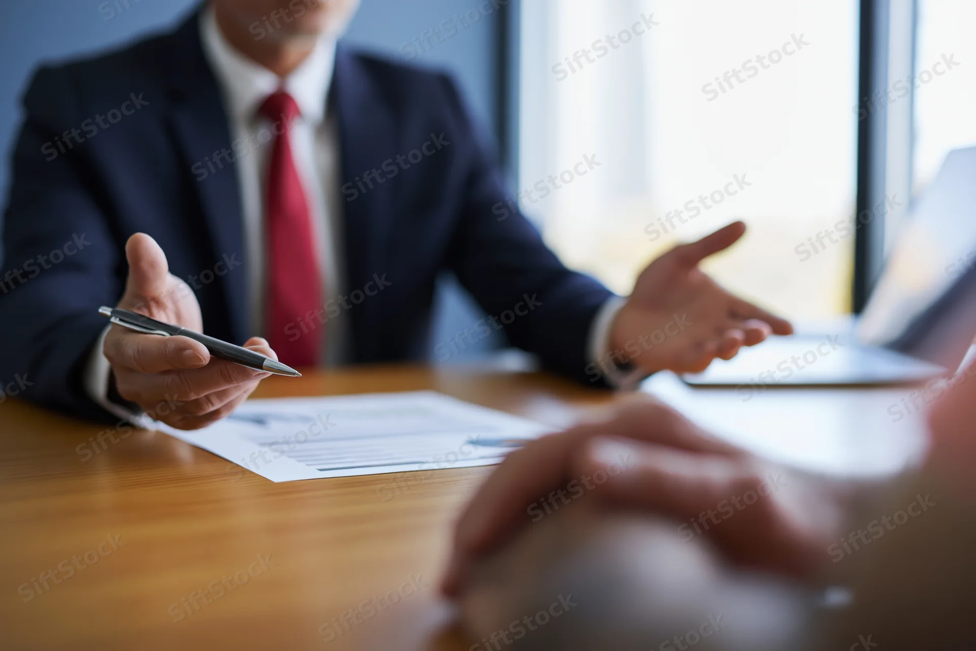 Businessman in suit holding pen during meeting at office desk with documents and laptop