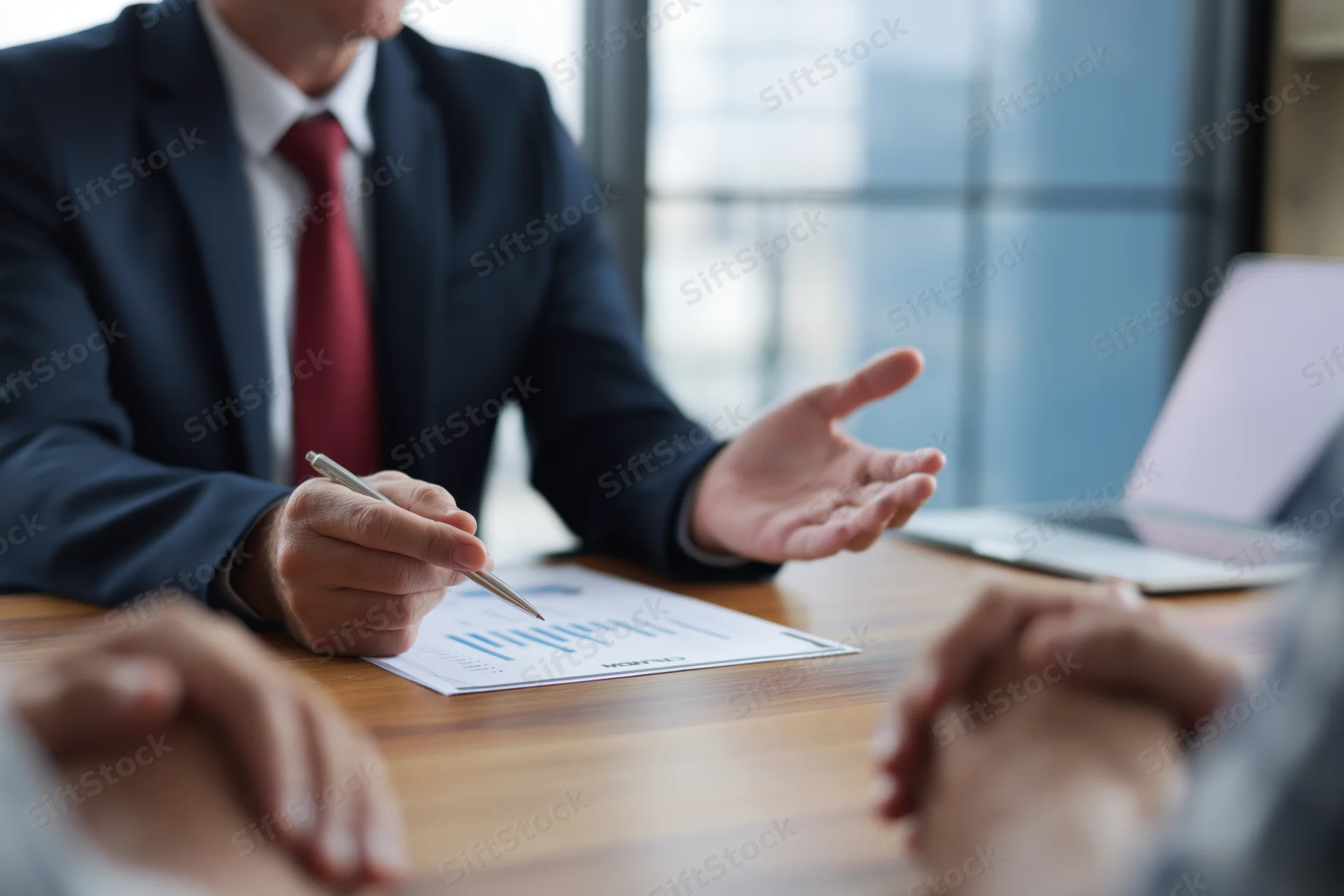 Businessman in suit holding pen over document during meeting at office desk