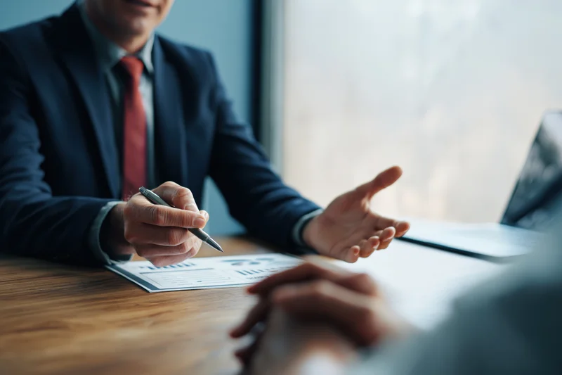 Businessman in suit holding pen and gesturing during meeting at office desk
