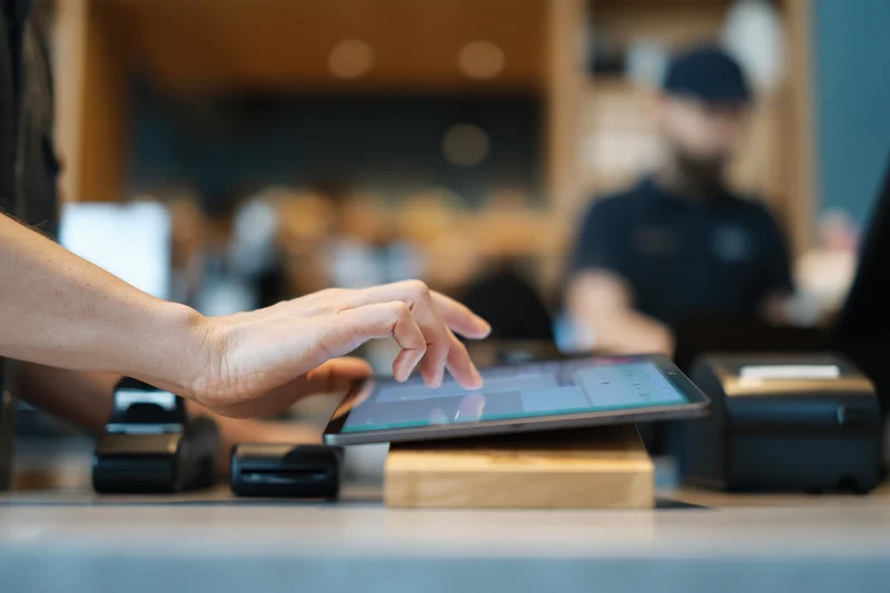 Cashier's hand tapping tablet point-of-sale screen at store counter