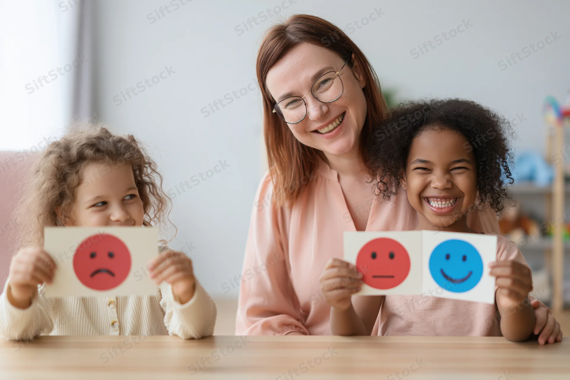 Child therapist smiling with two children holding emotion cards at table