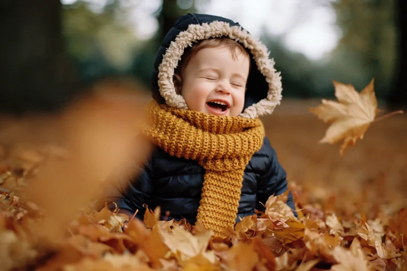 Toddler laughing in a pile of autumn leaves outdoors