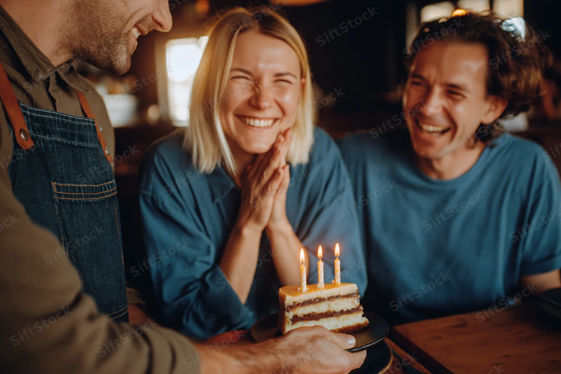 Waiter presenting birthday cake slice to smiling woman and man at restaurant table