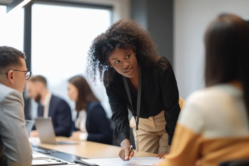 Young black woman leaning over conference table during business meeting in modern office