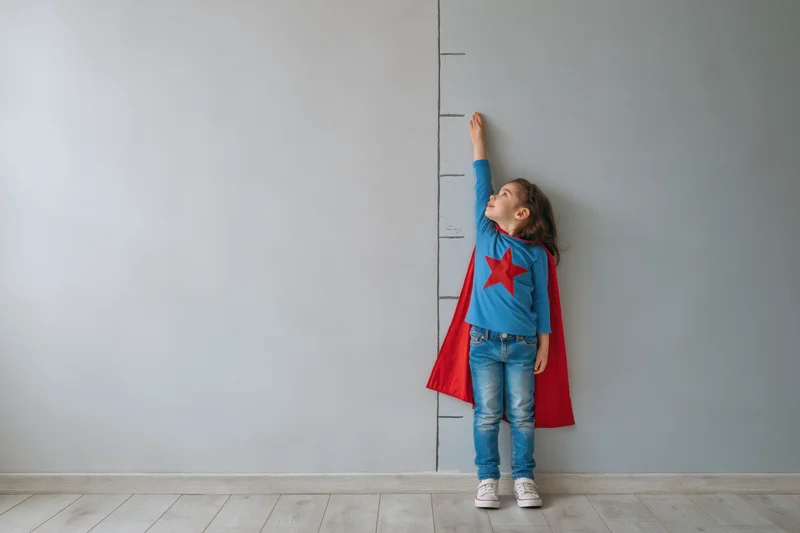 Young girl in superhero costume reaching upward to measure height on wall