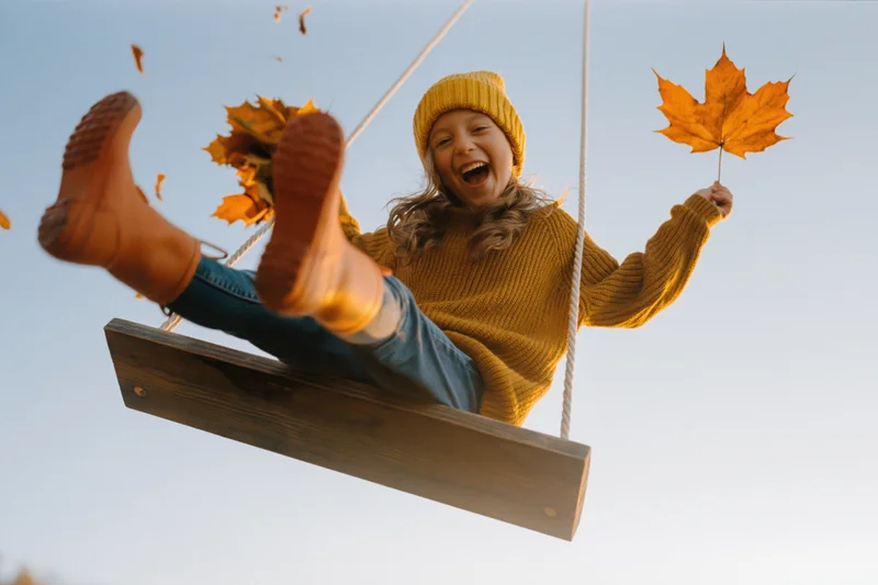 Young girl laughing on wooden swing holding autumn leaf outdoors