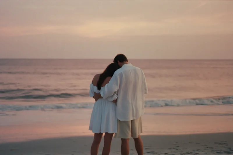 Young couple embracing on beach at sunset facing ocean