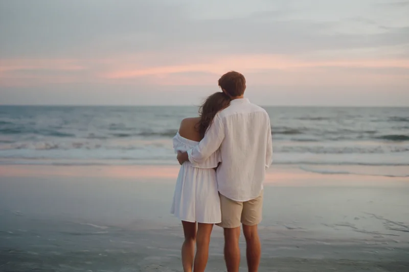 Young couple embracing on a beach at sunset facing the ocean