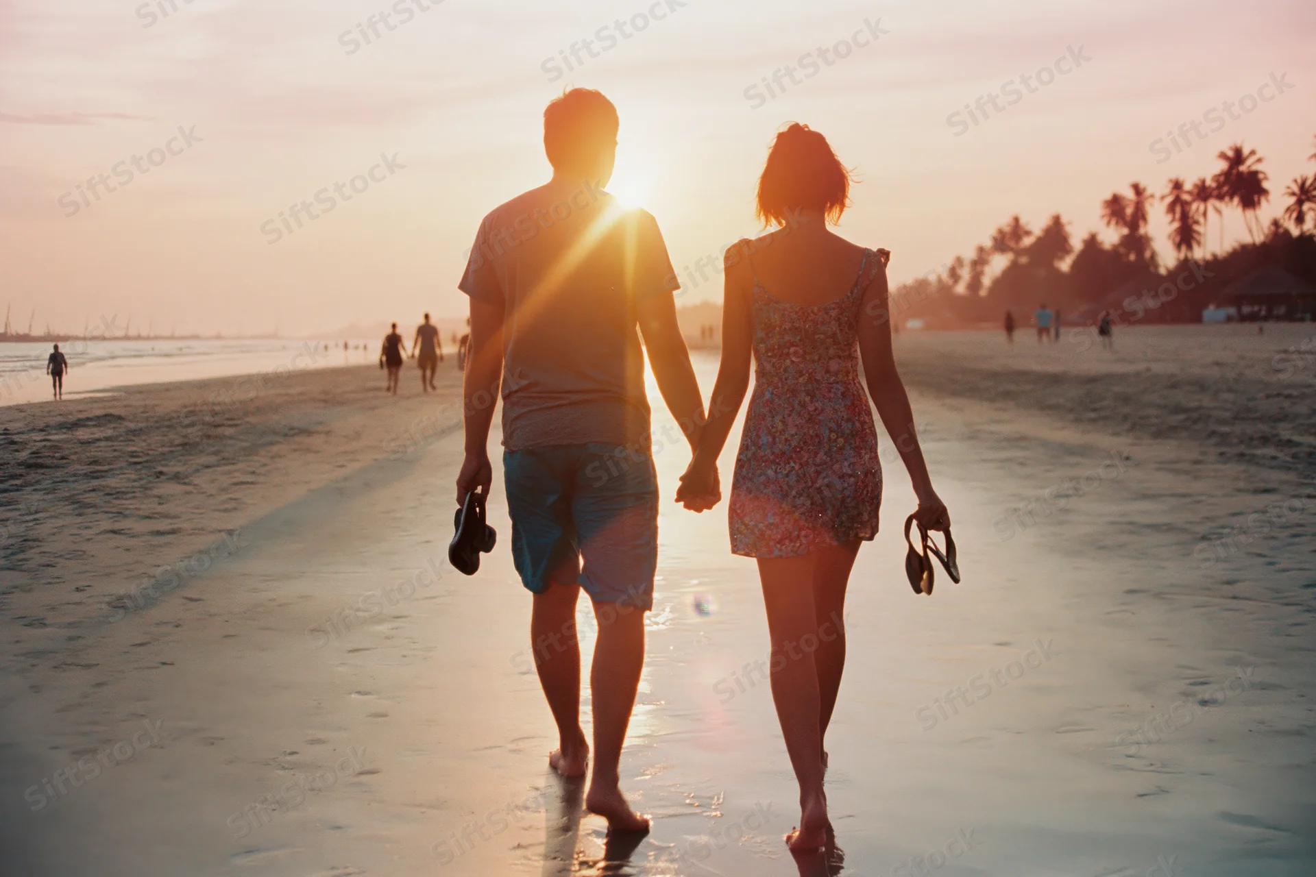 Couple holding hands walking barefoot along wet beach at sunset