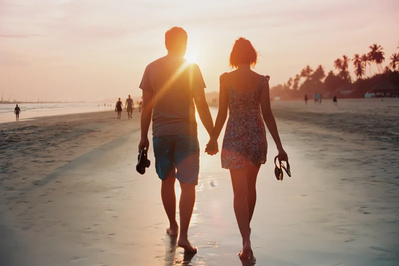 Couple holding hands walking barefoot along wet beach at sunset