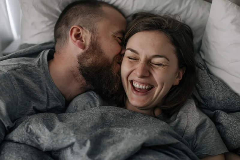 Bearded man kissing woman who is laughing in bed together