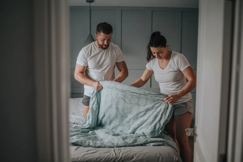 Young couple making bed together in bedroom morning