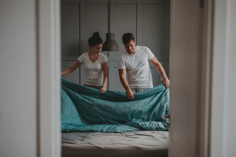 Young couple making bed together in bedroom morning
