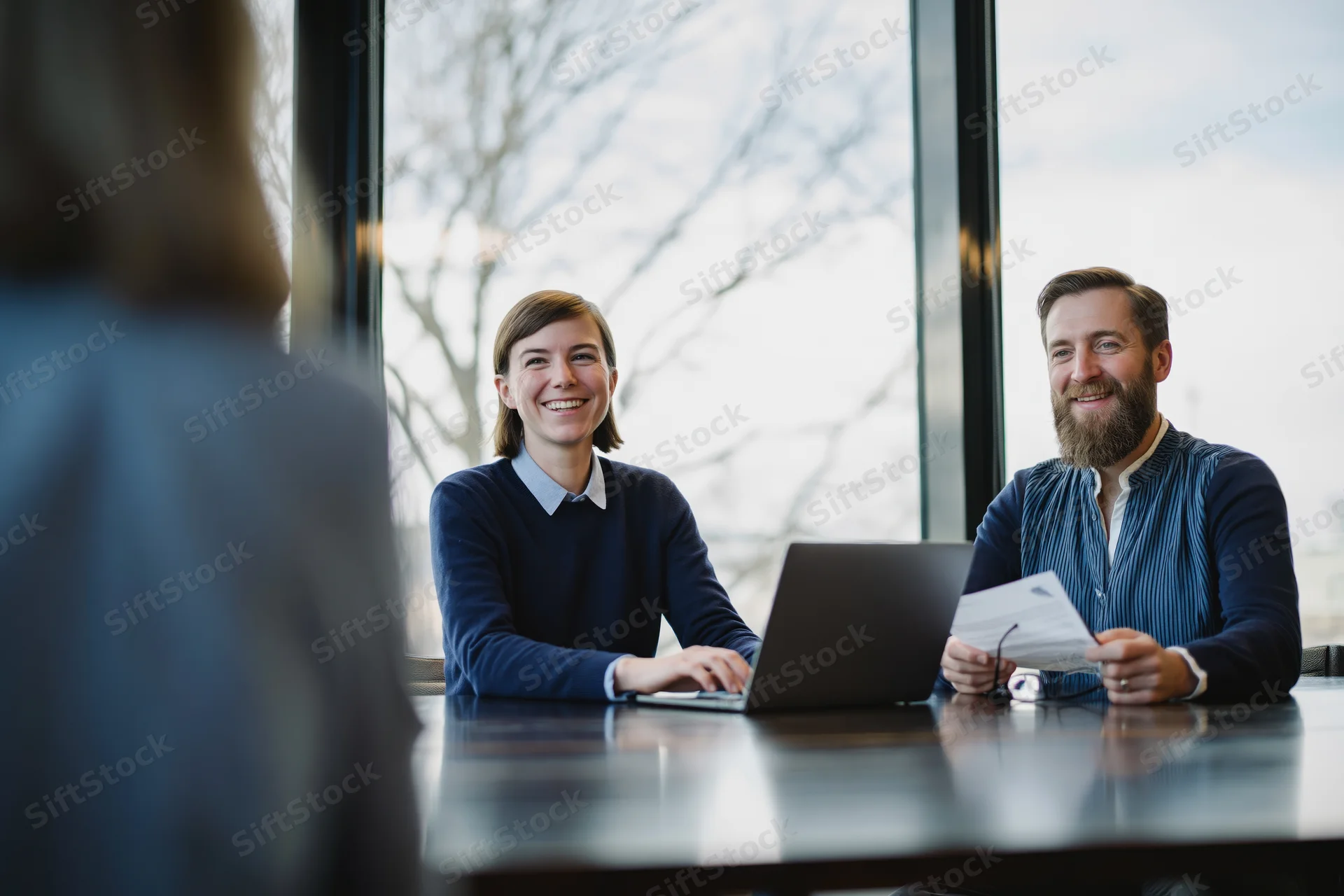 Two professionals smiling during a meeting at a conference table by a window