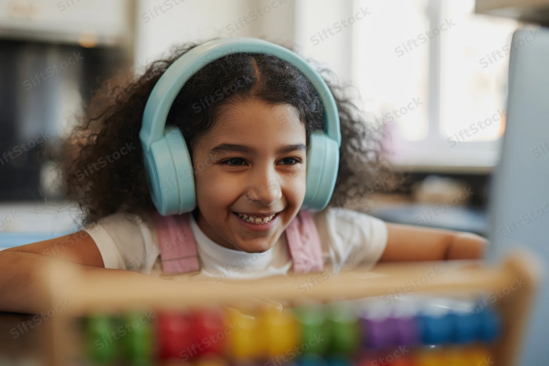 Young girl smiling while wearing headphones and looking at laptop screen at home desk
