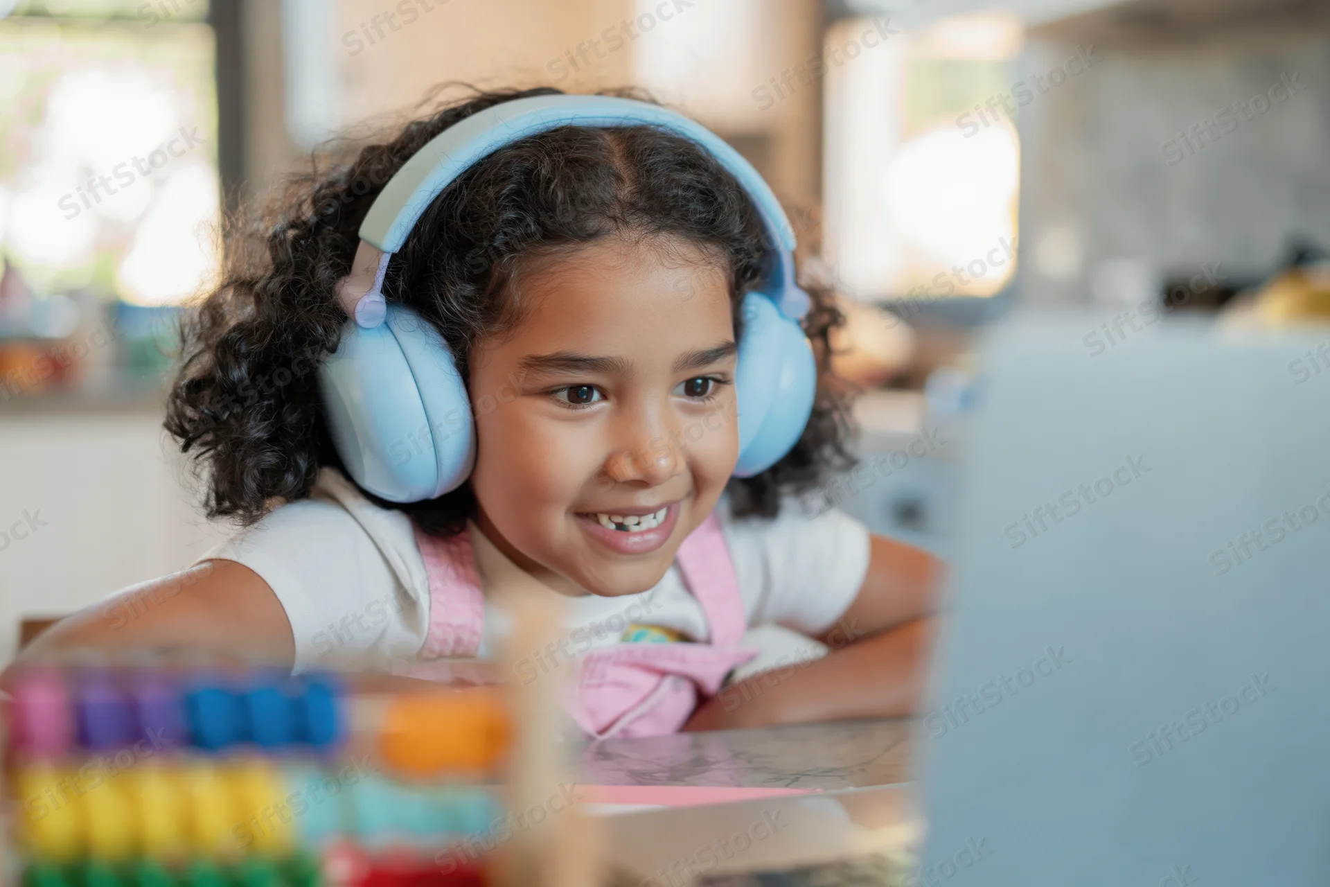 Young girl smiling while using laptop with headphones at home desk