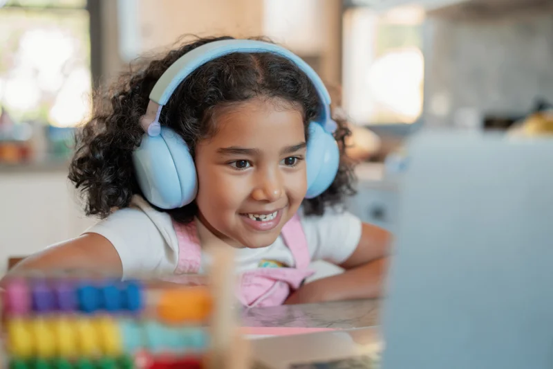 Young girl smiling while using laptop with headphones at home desk