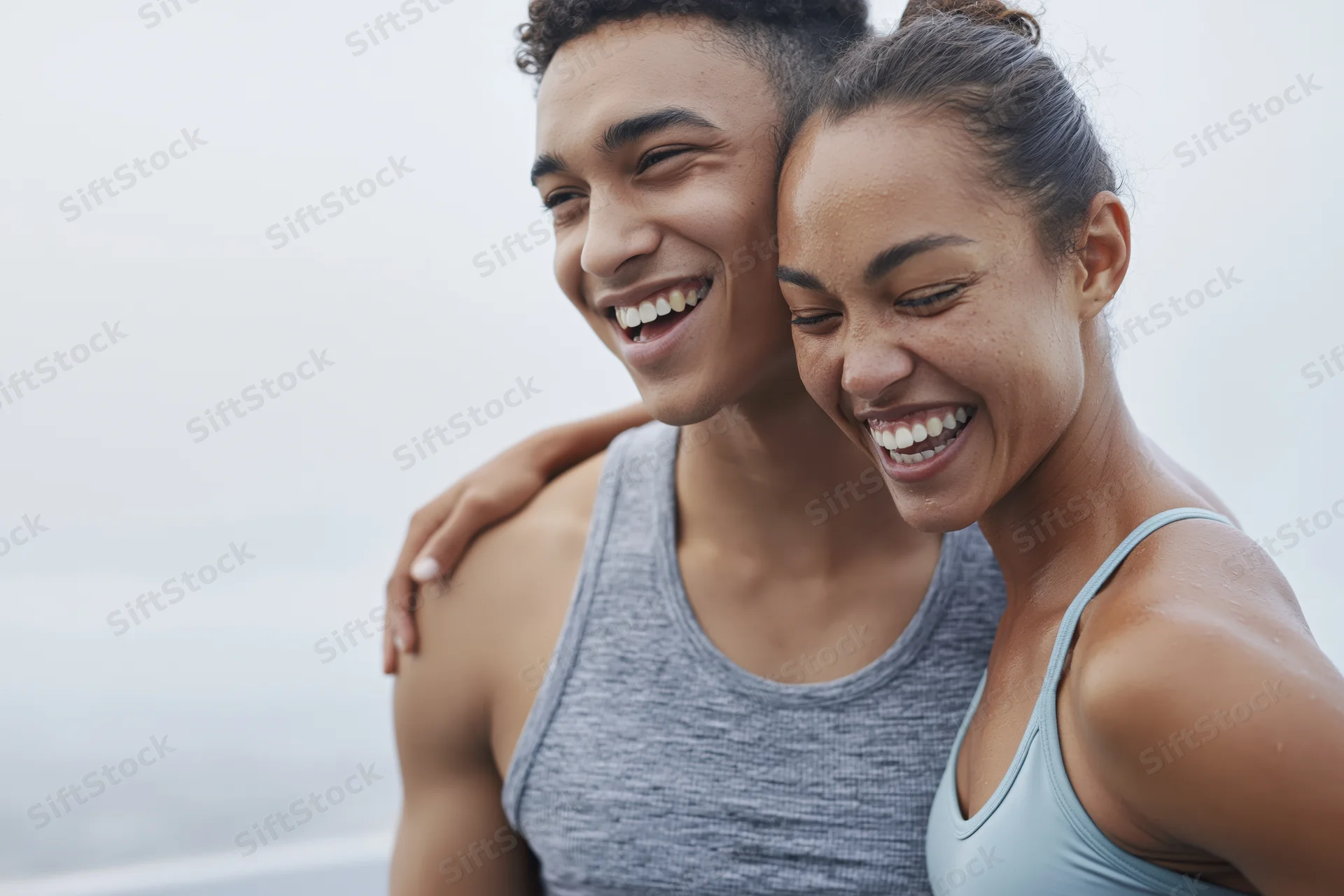 Young interracial couple laughing together in workout clothes outdoors near the ocean