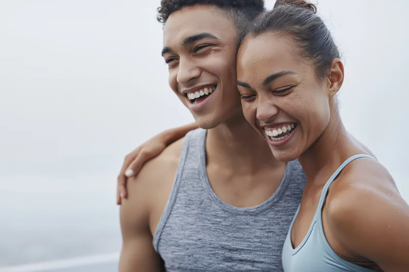 Young interracial couple laughing together in workout clothes outdoors near the ocean