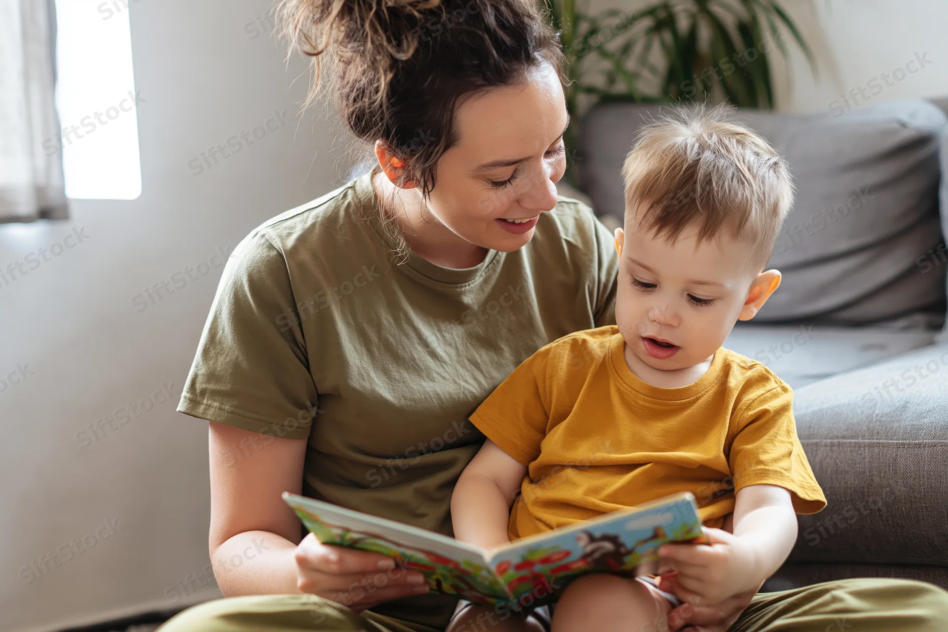 Mother reading a book with her toddler son on the floor in a living room