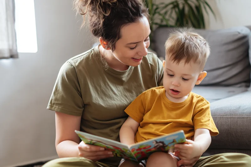 Mother reading a book with her toddler son on the floor in a living room