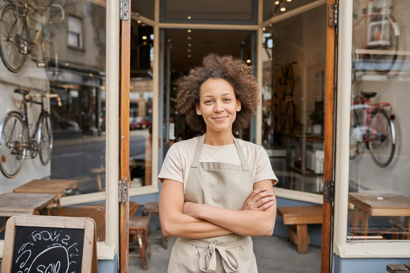Woman in beige apron standing with arms crossed at entrance of bicycle shop