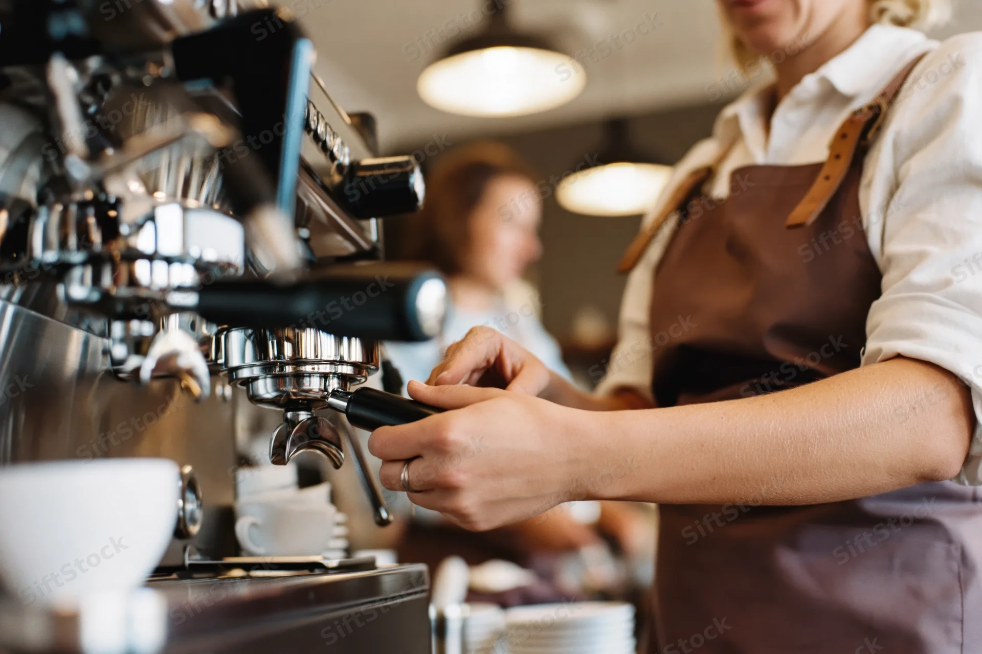 Woman barista operating chrome espresso machine in cafe interior