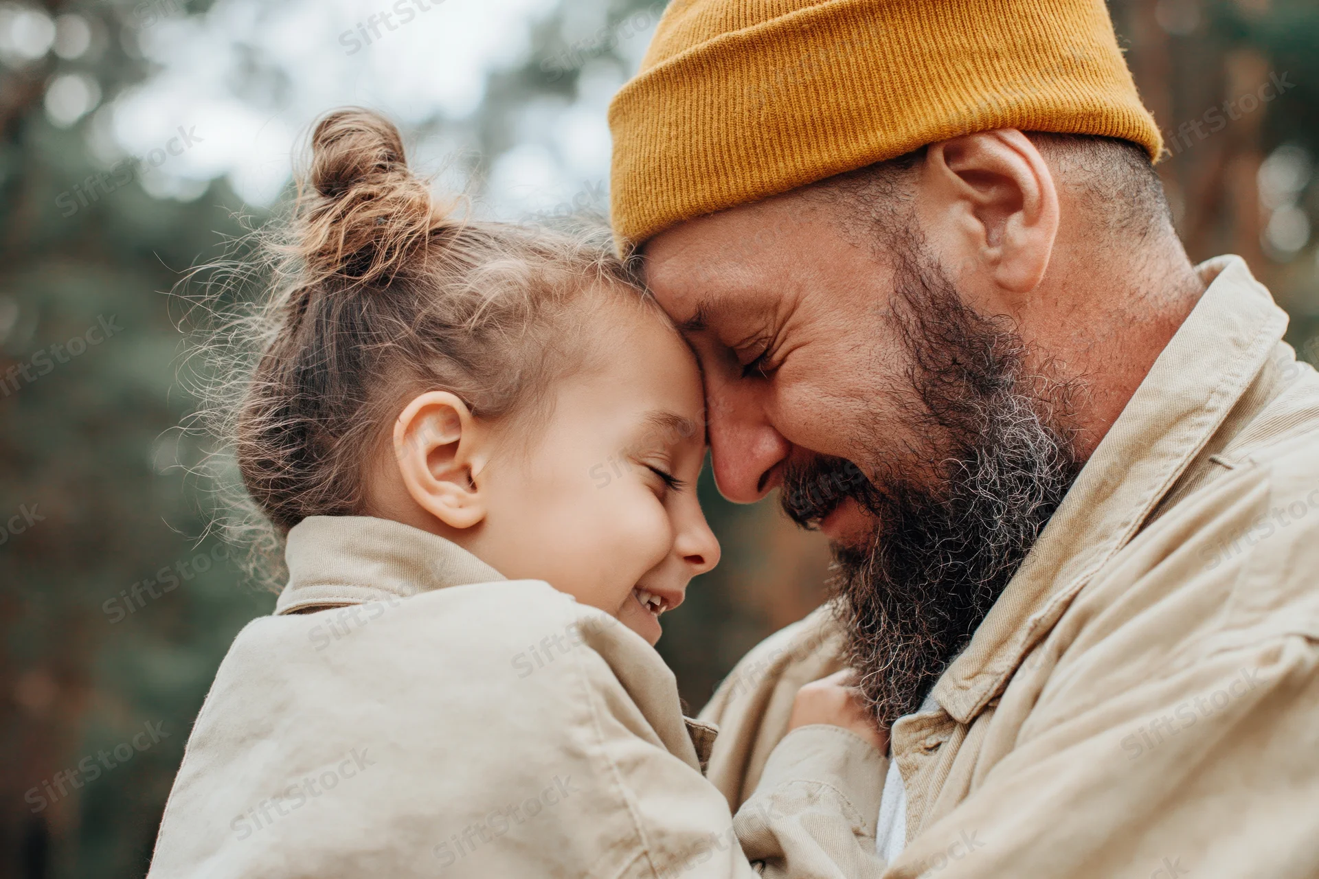 Bearded father and young daughter touching foreheads while smiling in a forest setting