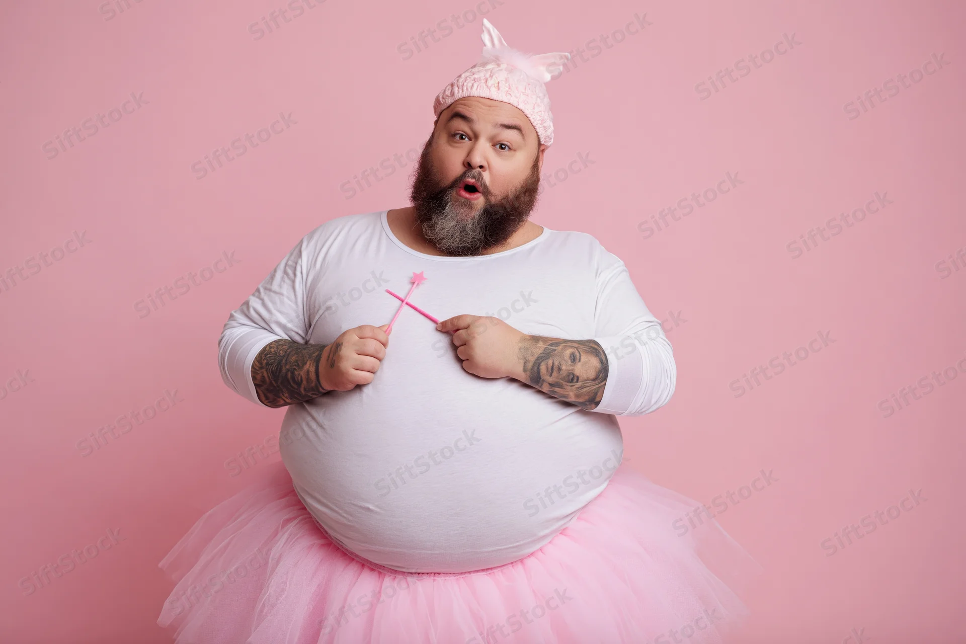 Bearded heavyset man in fairy godmother costume with pink tutu and wand, surprised expression against pink background