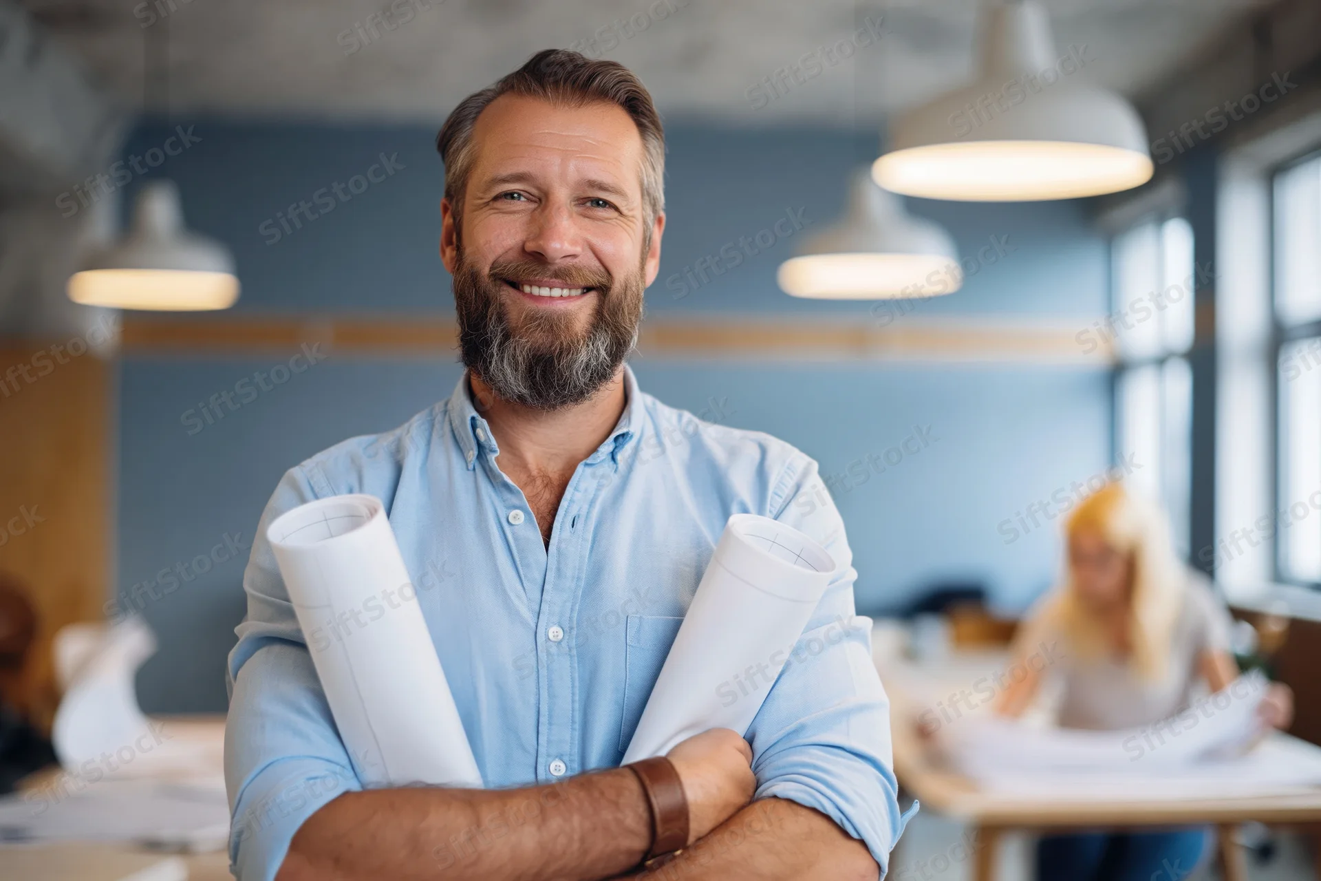 Bearded middle-aged architect smiling with rolled blueprints in modern office