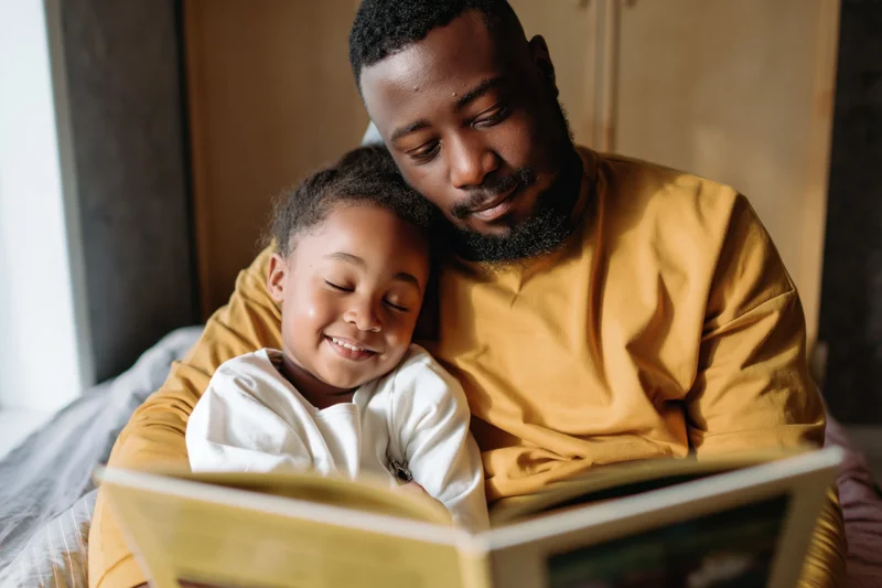 Black father reading a picture book to his young daughter