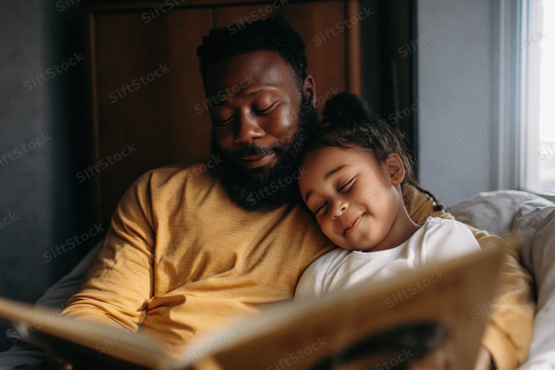 Black father reading a picture book to his young daughter in bed