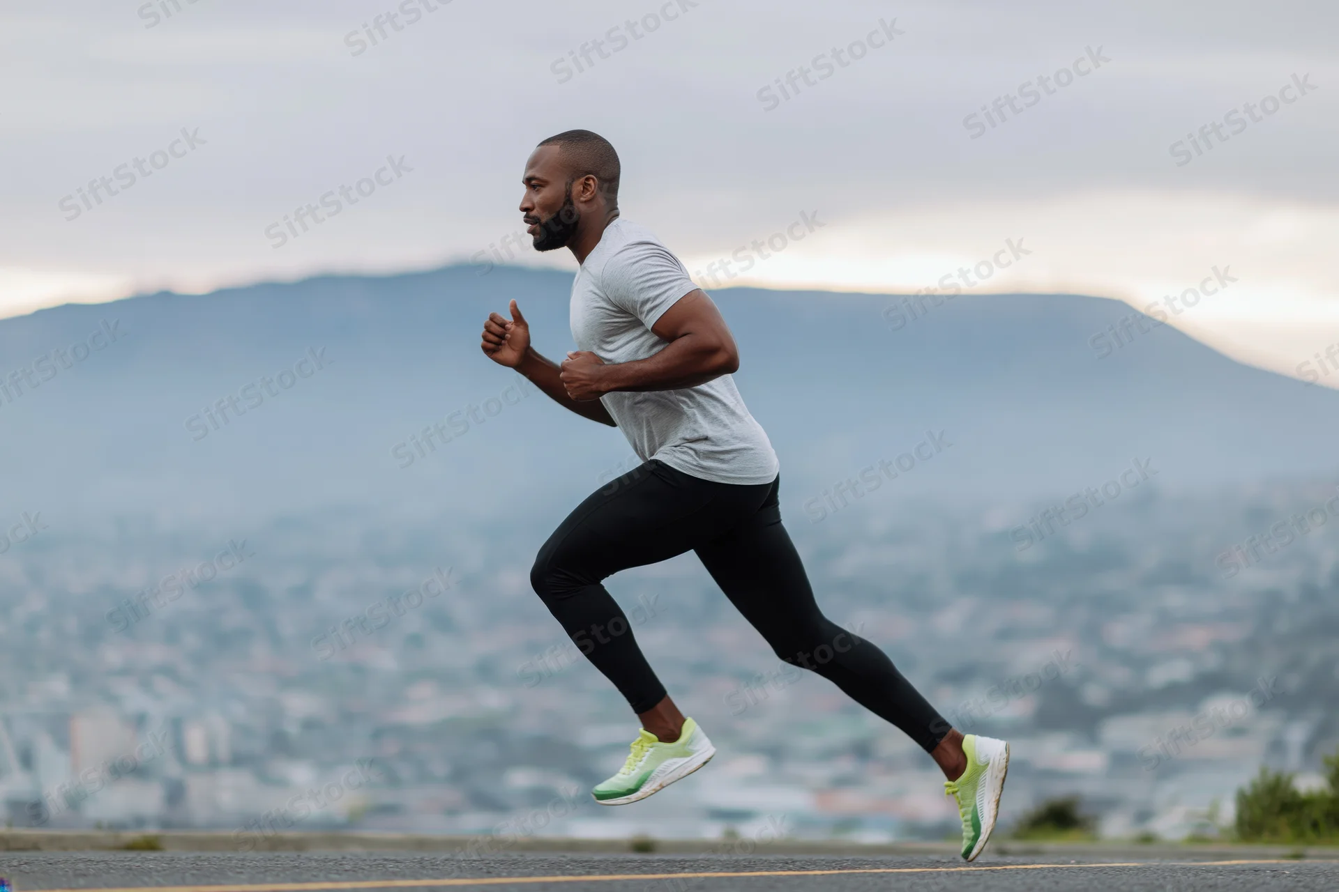 Black man running midstride on a hilltop road overlooking a city and mountains