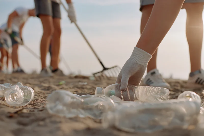 Volunteer's gloved hand picking up plastic bottles on sandy beach during cleanup event