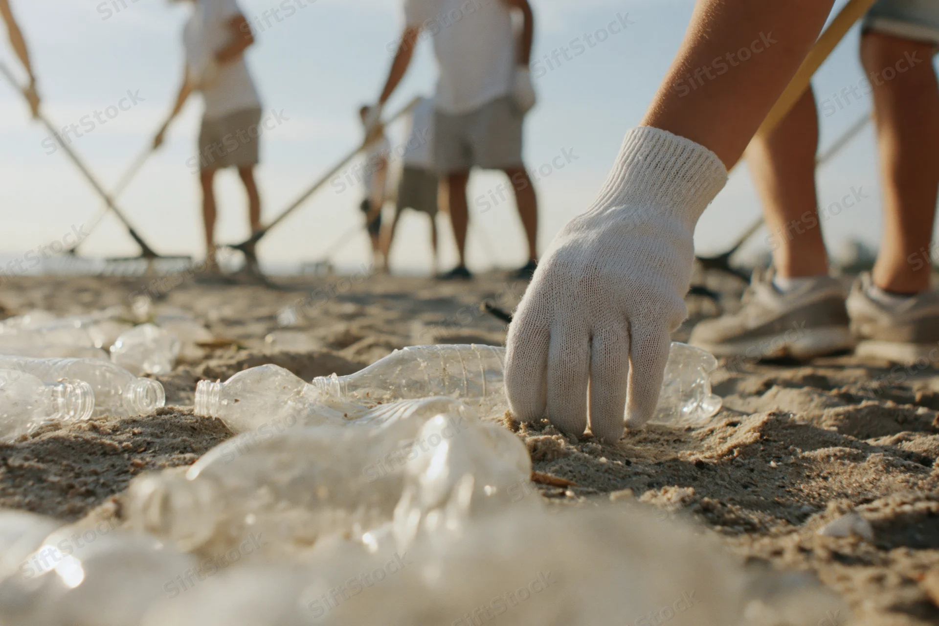 Volunteer's gloved hand picking up plastic bottles on sandy beach during cleanup event