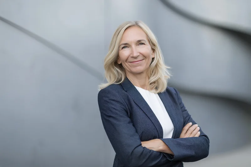 Confident middle-aged businesswoman standing with arms crossed in front of modern gray concrete building exterior