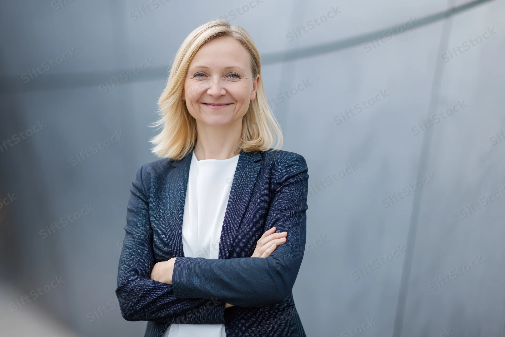 Confident middle-aged businesswoman standing with arms crossed in front of modern glass building exterior