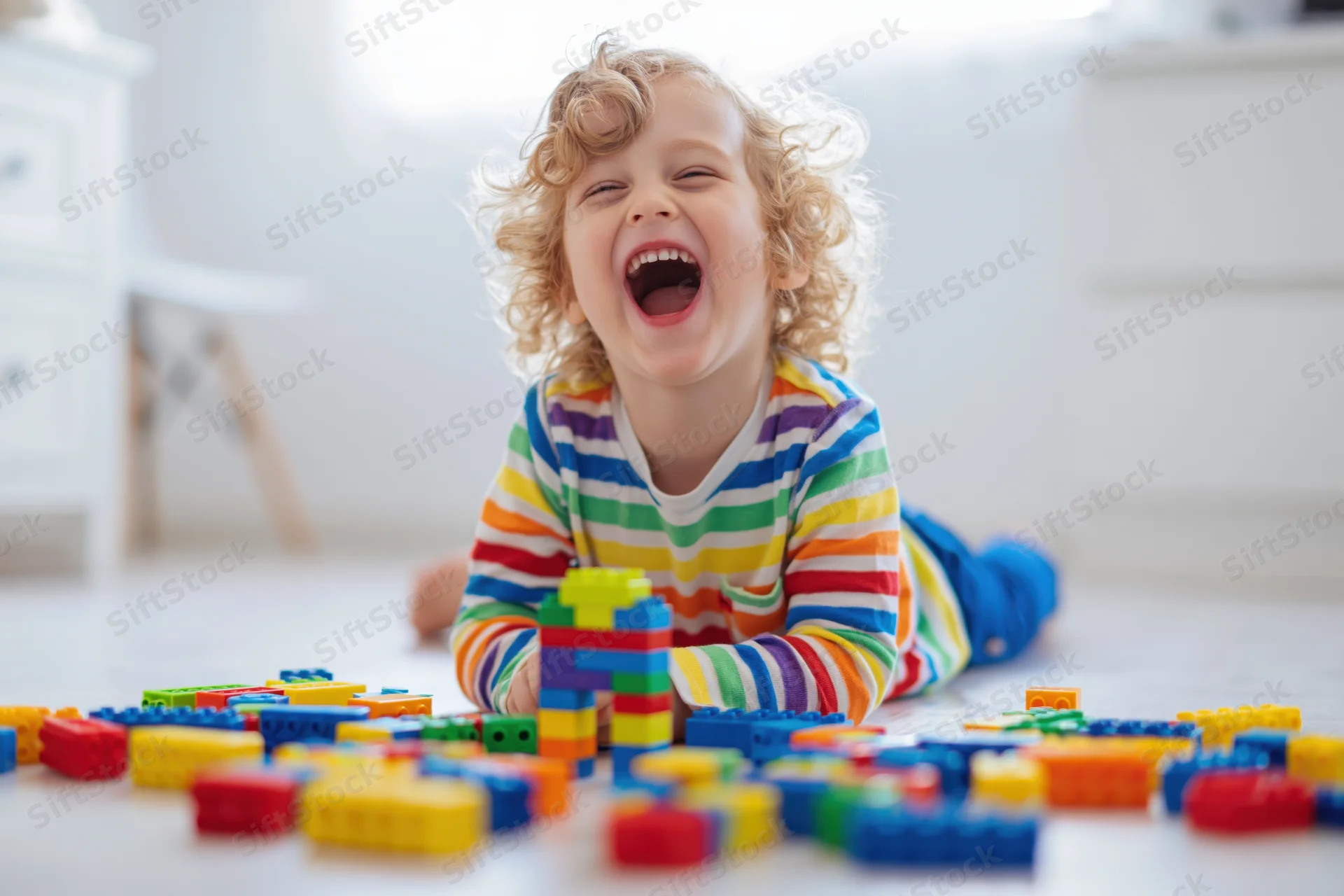 Curly blond toddler laughing while playing with colorful building blocks on the floor