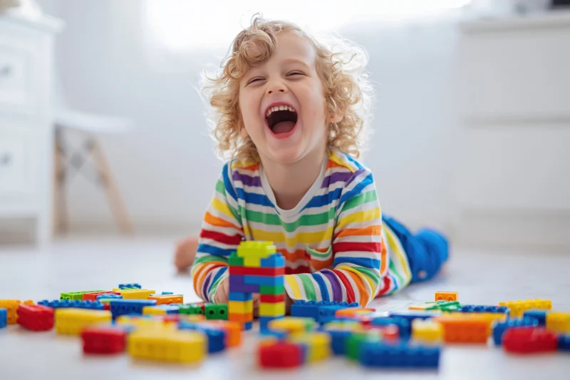 Curly blond toddler laughing while playing with colorful building blocks on the floor