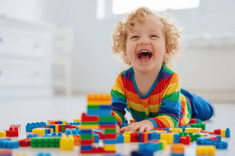 Curly blond toddler laughing while playing with colorful building blocks on the floor