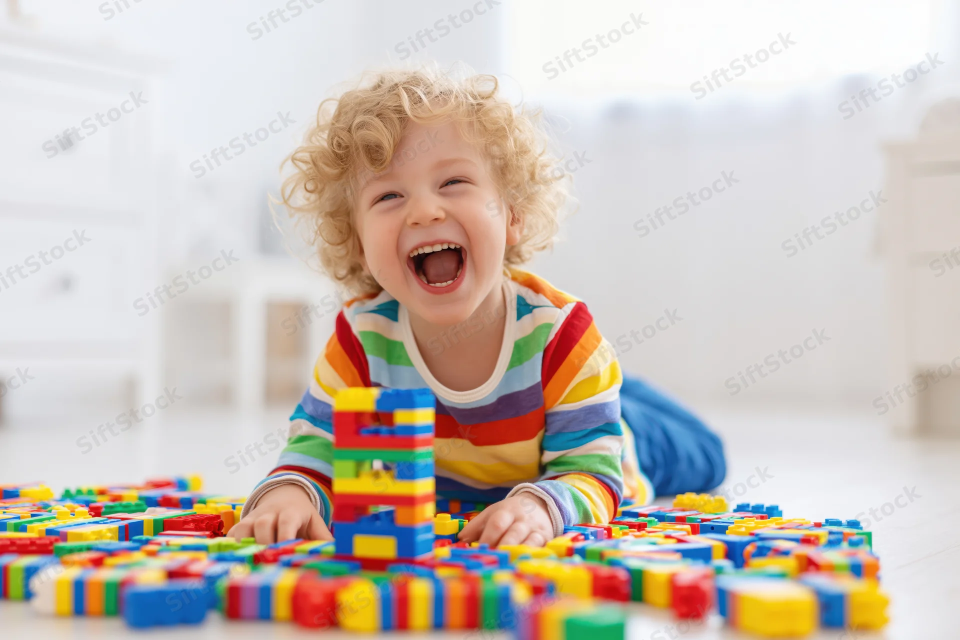Curly blond toddler laughing while playing with colorful building blocks on the floor